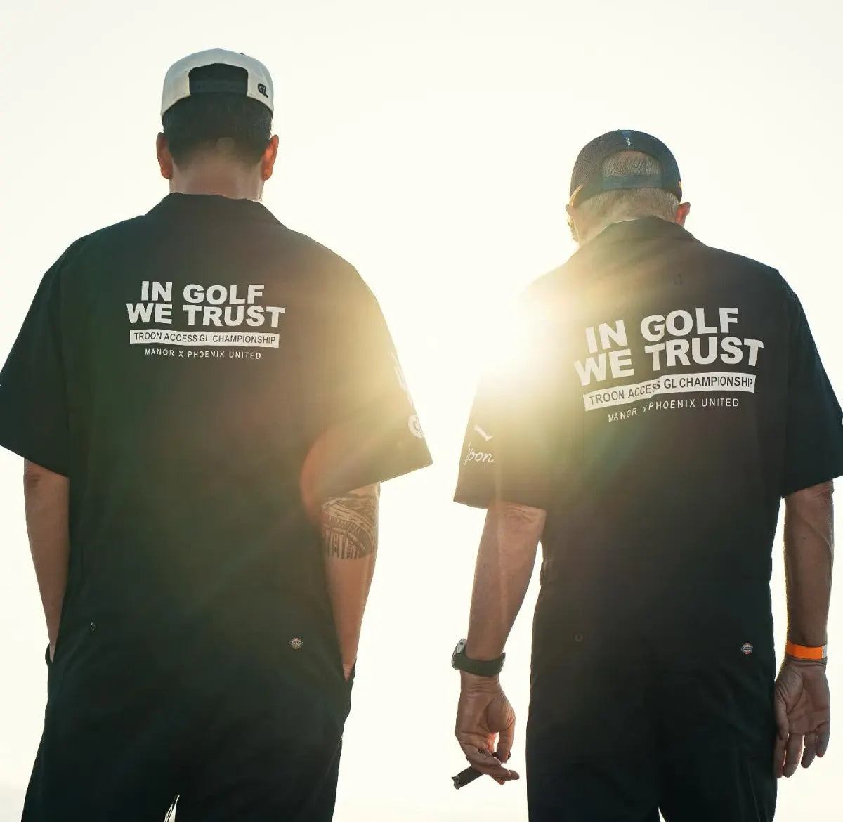 Two players silhouetted in 'In Golf We Trust' tees at dusk